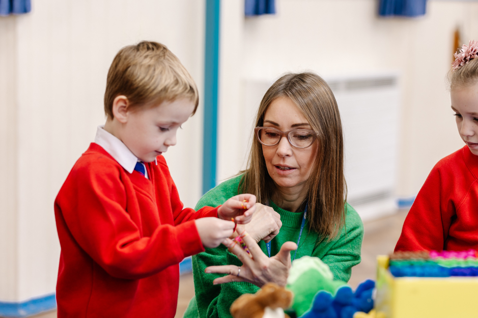 A female teacher helping a child with a red jumper to crochet.